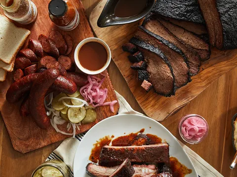Overhead spread of sliced brisket, house sausage, pork ribs, pickles and white bread on wood boards at Lewis Barbecue in Charleston