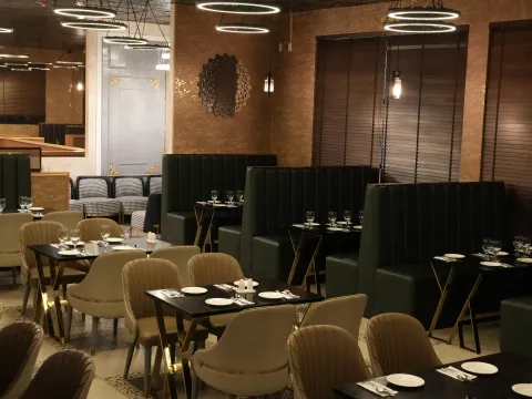 The dining room at Bombay Bistro in Redmond, with set tables, tall green upholstered booths, gold accents and ring pendant lights