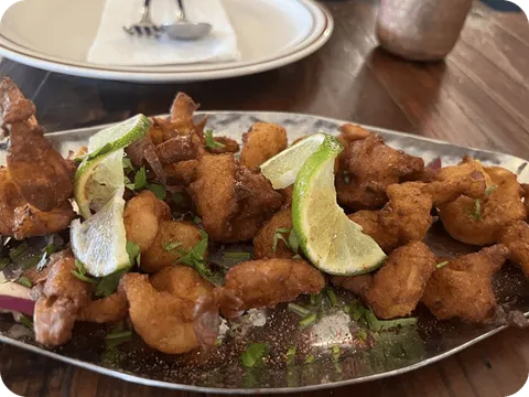 Prawns koliwada — batter-fried prawns garnished with lime wedges and cilantro on a metal platter at Swaraj India, Santa Clara