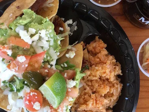 A plate of Taqueria El Bajio tacos dorados topped with guacamole, queso, tomato and jalapeño, served with Mexican rice and salsa