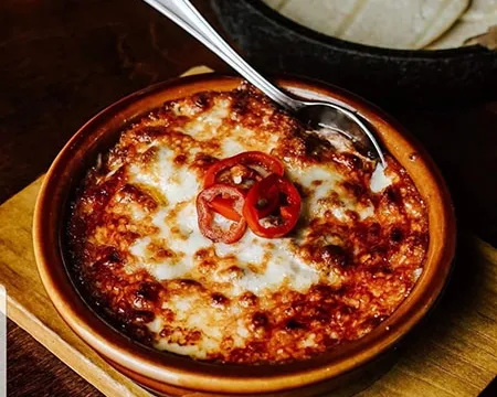 Baked queso fundido with sliced peppers at Momocho